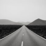 A long two-lane road stretches from the foreground to the mountains in the distance. It symbolizes the long road to an indie author book launch.