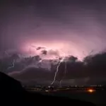 Violet-purple sky, lightning cracking over a lit-up town at night. The energy of pre-launch, for romantasy books in 2026, and for the fourth wing book 4 release date!