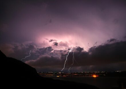 Violet-purple sky, lightning cracking over a lit-up town at night. The energy of pre-launch, for romantasy books in 2026, and for the fourth wing book 4 release date!