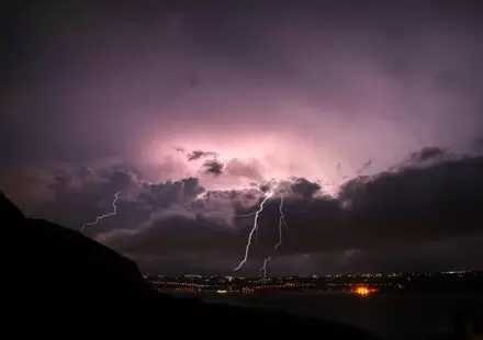 Violet-purple sky, lightning cracking over a lit-up town at night. The energy of pre-launch, for romantasy books in 2026, and for the fourth wing book 4 release date!