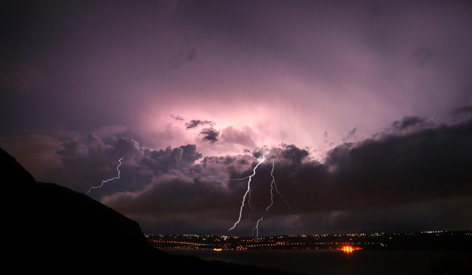 Violet-purple sky, lightning cracking over a lit-up town at night. The energy of pre-launch, for romantasy books in 2026, and for the fourth wing book 4 release date!