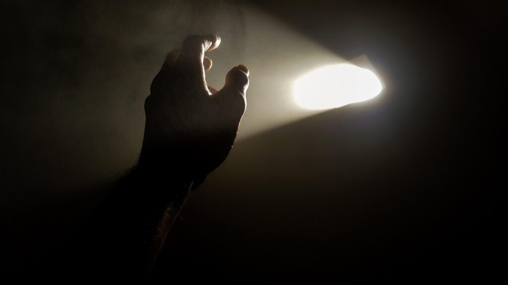 In the darkness, a hand reaches up to a hole in a wall through which white light pours through. The dark wall symbolizes depression diguised as writer's block.