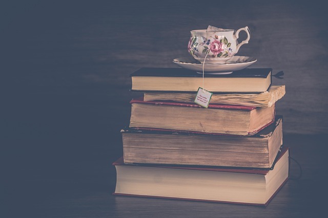 A stack of books with a teacup and saucer on top. the books look too old to be new romantasy releases for 2026, though. 